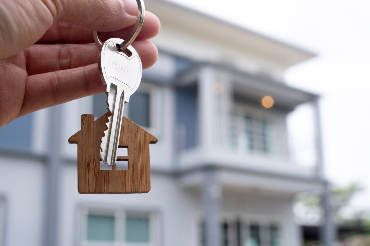 A person is holding a house key in front of a house