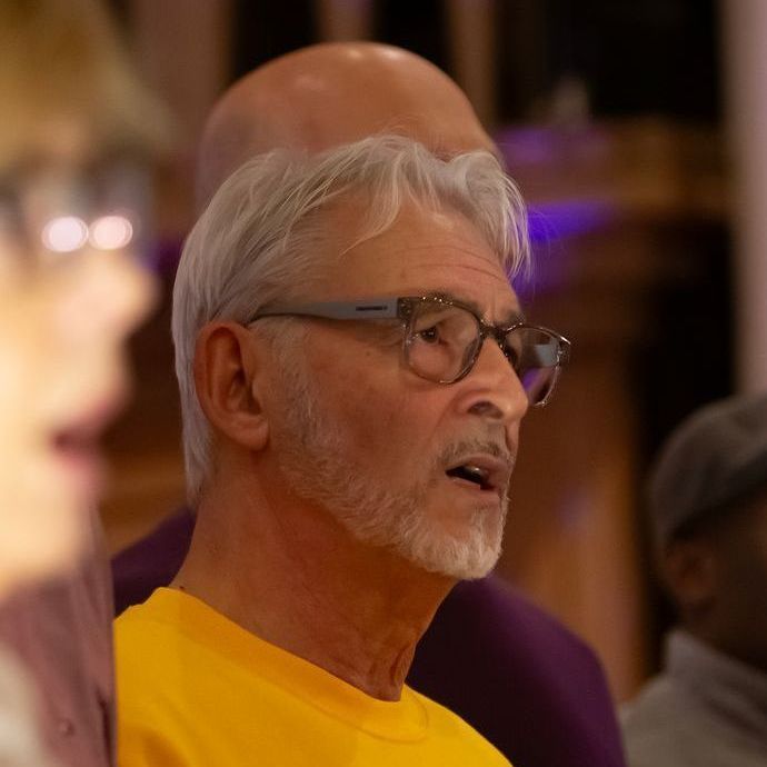 A man wearing glasses and a yellow shirt is singing