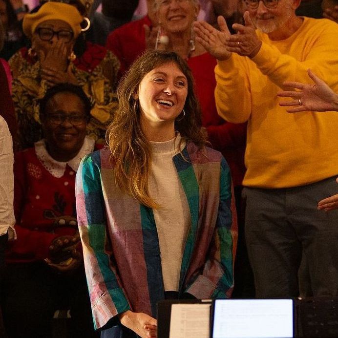 A woman in a bright, patterned jacket is smiling in front of a choir