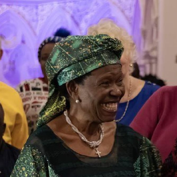 A woman wearing a green headscarf and a necklace is smiling