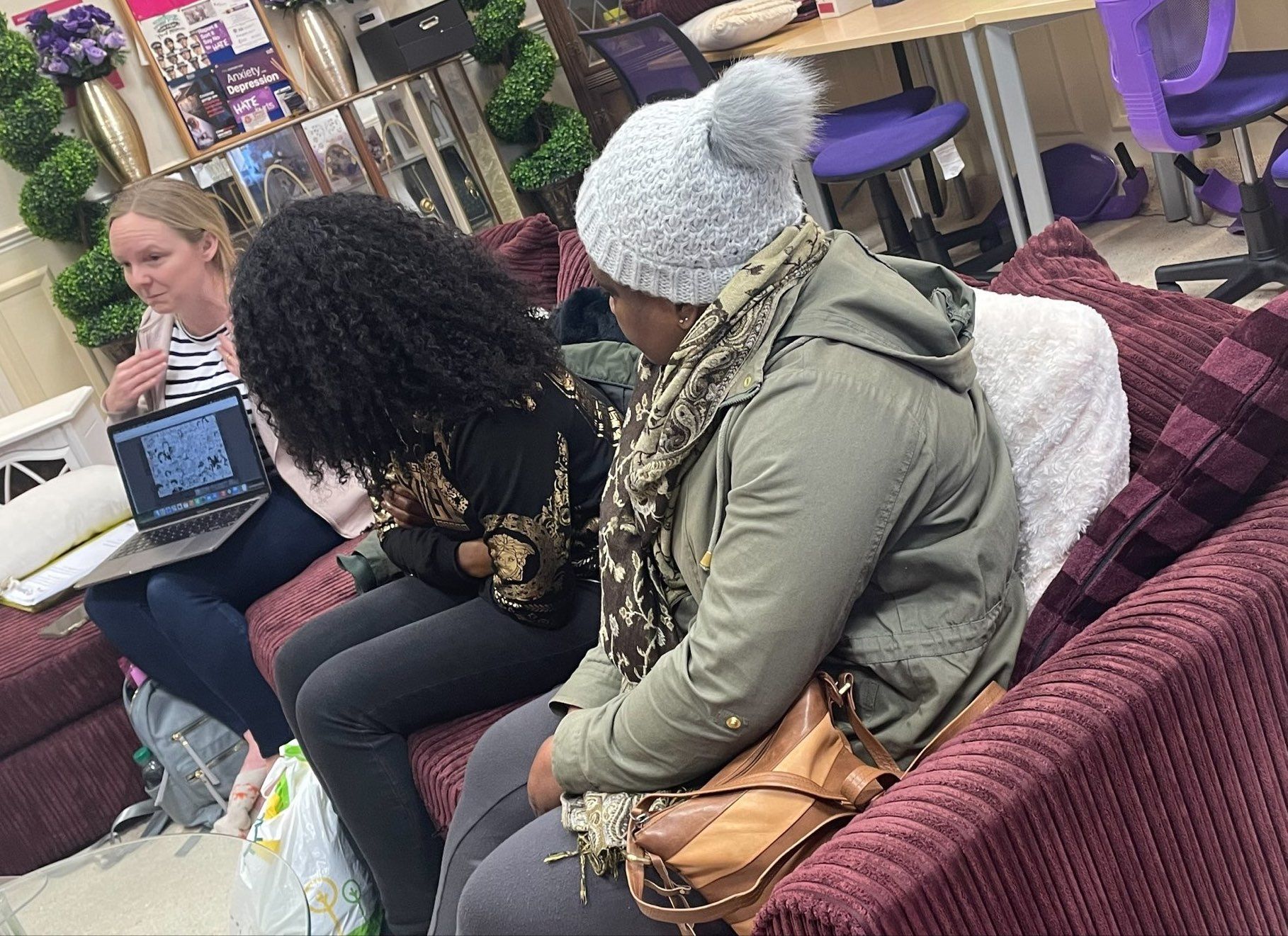 A group of women are sitting on a couch with laptops.