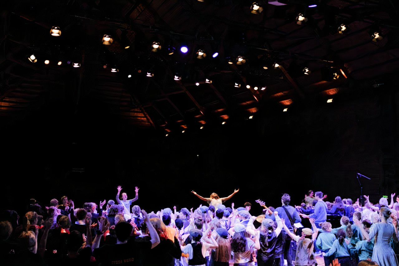 A large group of people are dancing on a stage in a dark room.