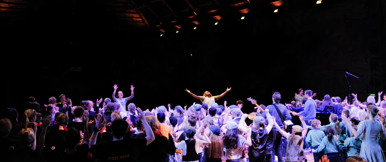 A large group of people are dancing on a stage in a dark room.
