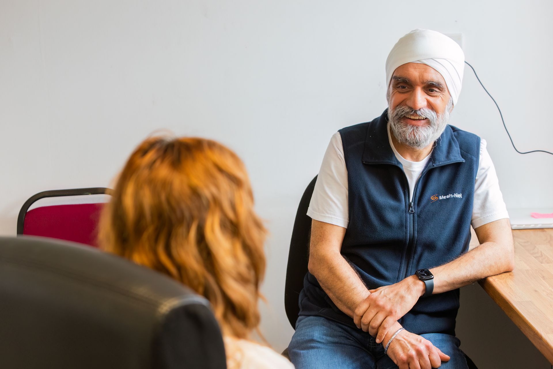 A man in a turban is sitting at a desk talking to a woman.