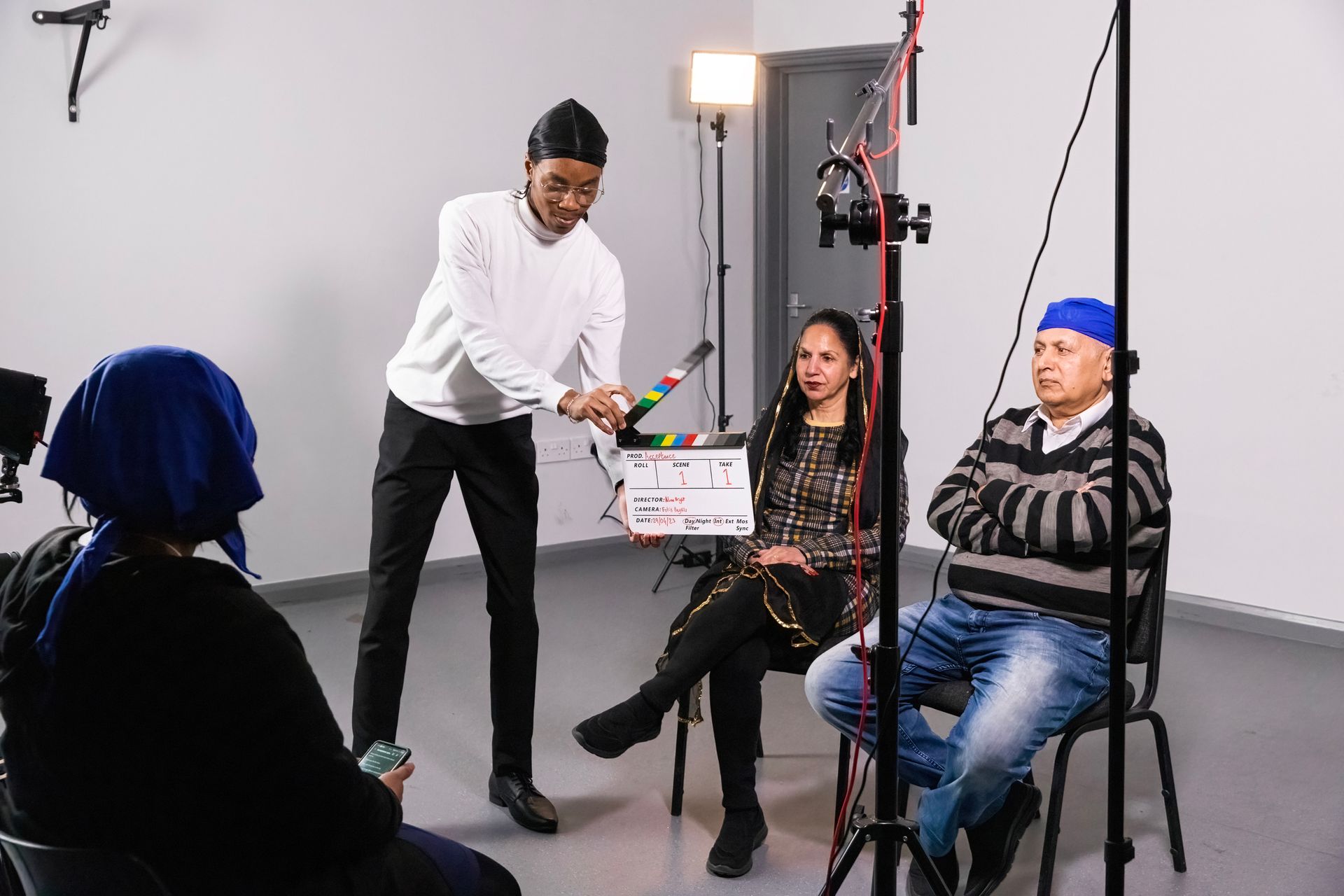 A man is holding a clapper board in front of a group of people sitting in chairs.