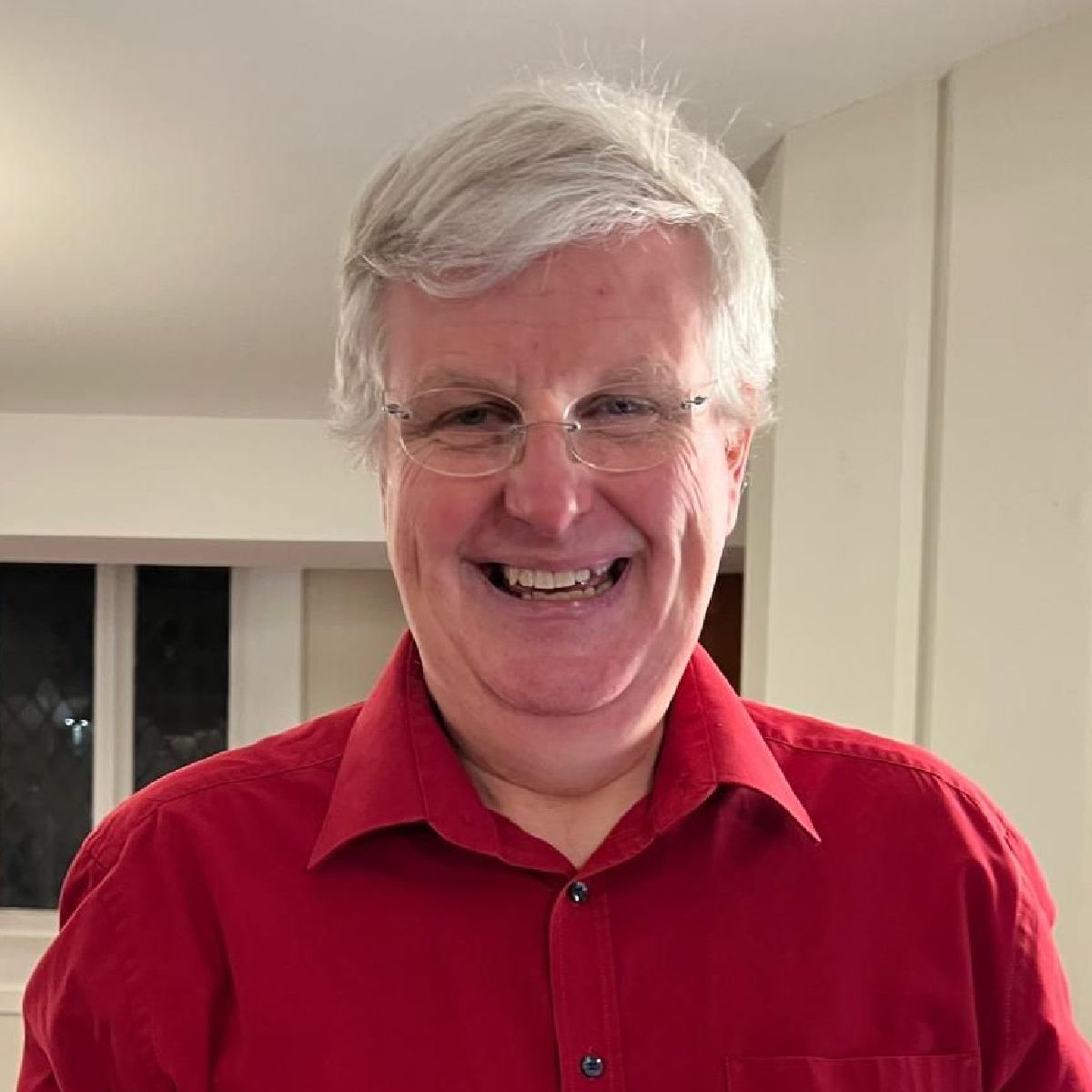 A man wearing glasses and a red shirt is smiling for the camera.