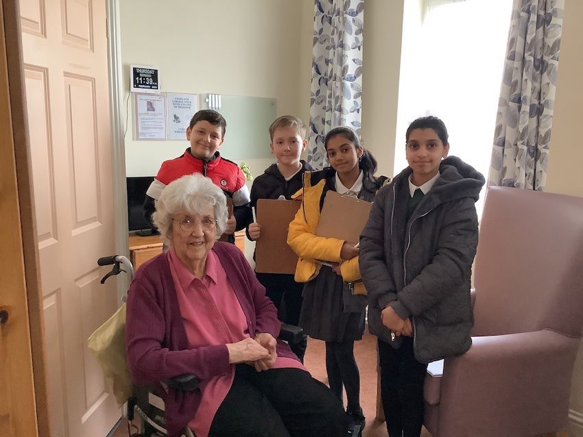 A group of children are standing around an elderly woman in a wheelchair.