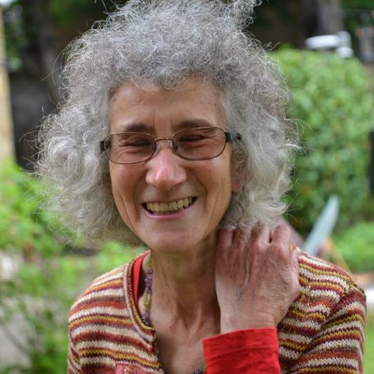 The woman is wearing glasses and a striped shirt and smiling.