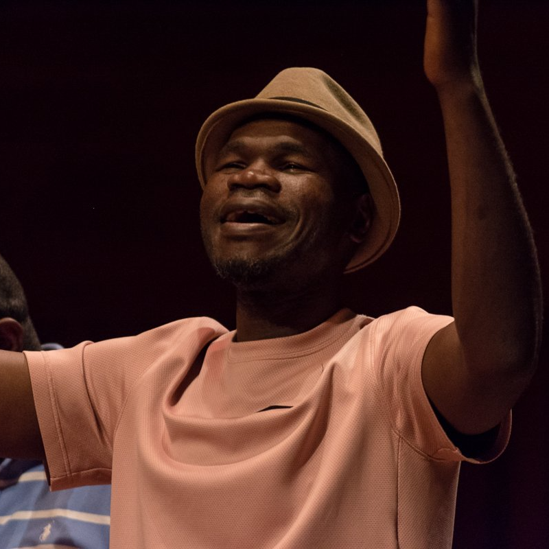 A man wearing a hat and a pink shirt is raising his arms in the air