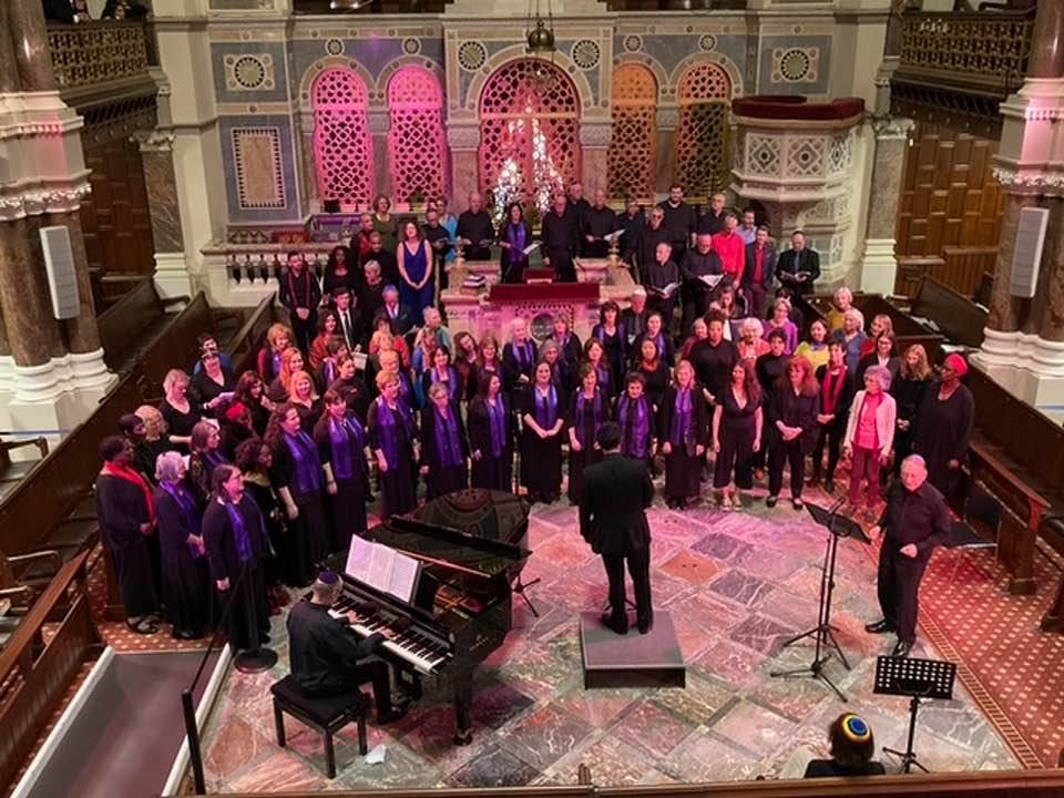 A large choir is singing in a church with a man playing a piano.
