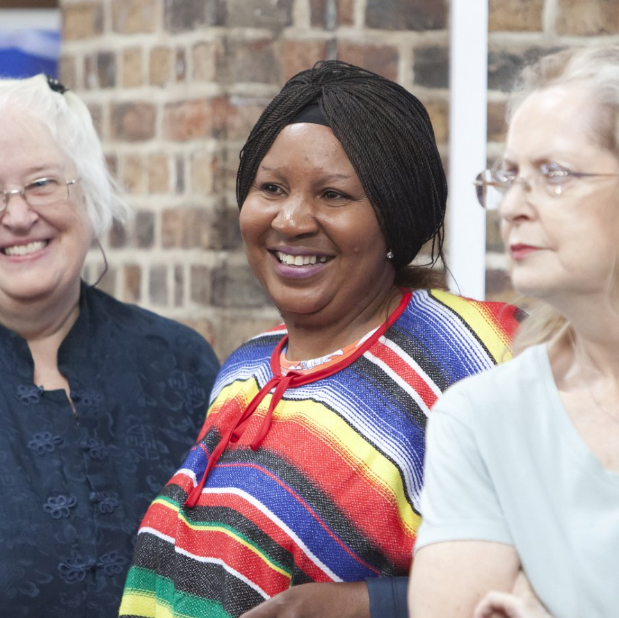 A woman wearing a black headscarf and colourful striped top smiles in a crowd