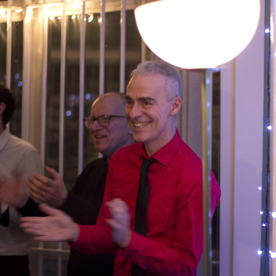 A man in a red shirt and black tie is smiling