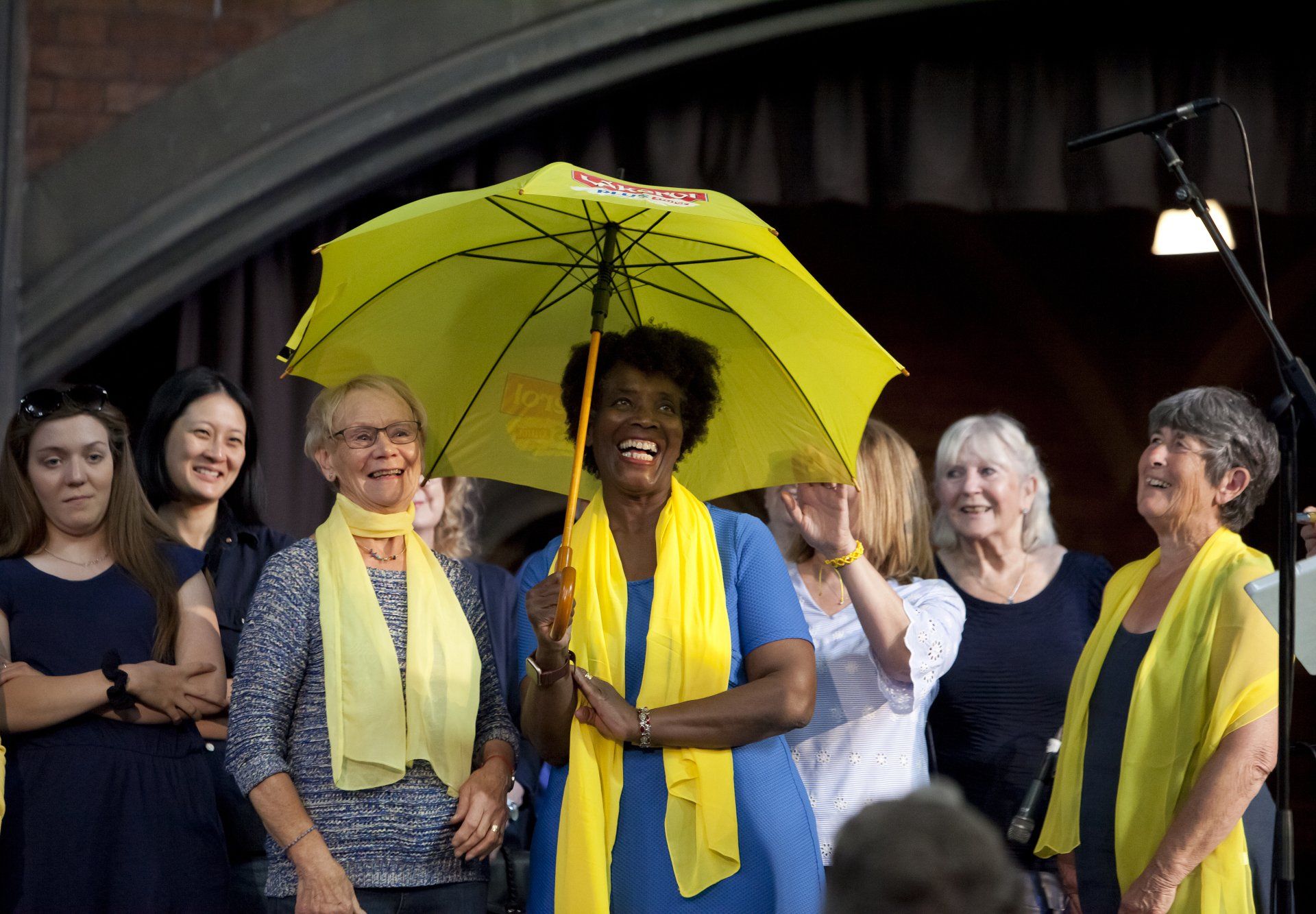 A woman in a blue dress is holding a yellow umbrella