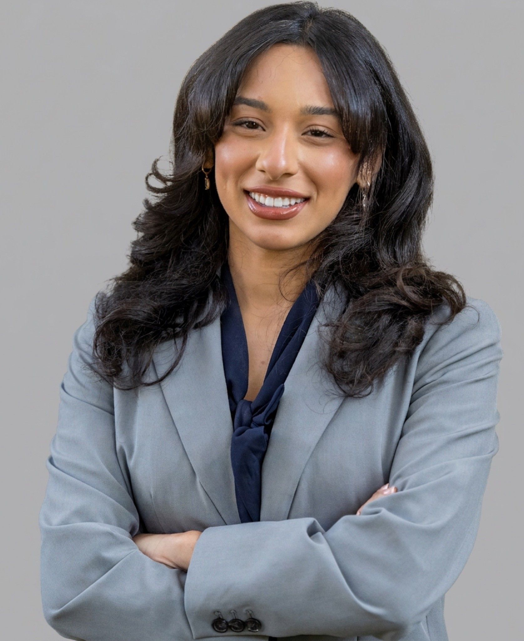 Smiling professional in a gray blazer with arms crossed against a plain background