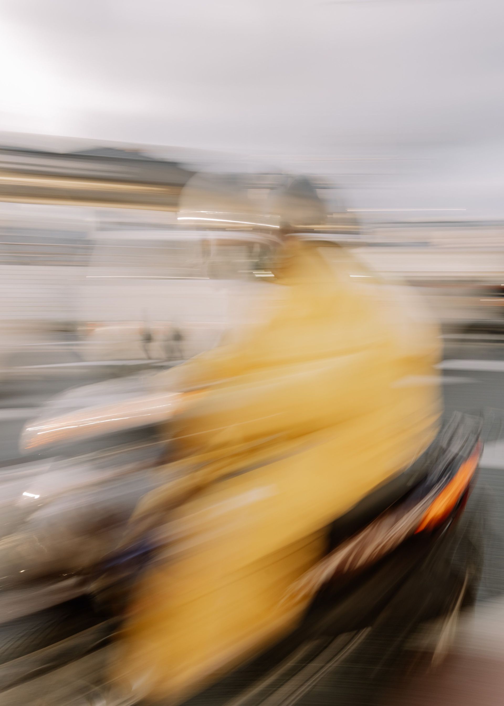 Blurred person in a yellow raincoat riding a scooter through a rainy street scene