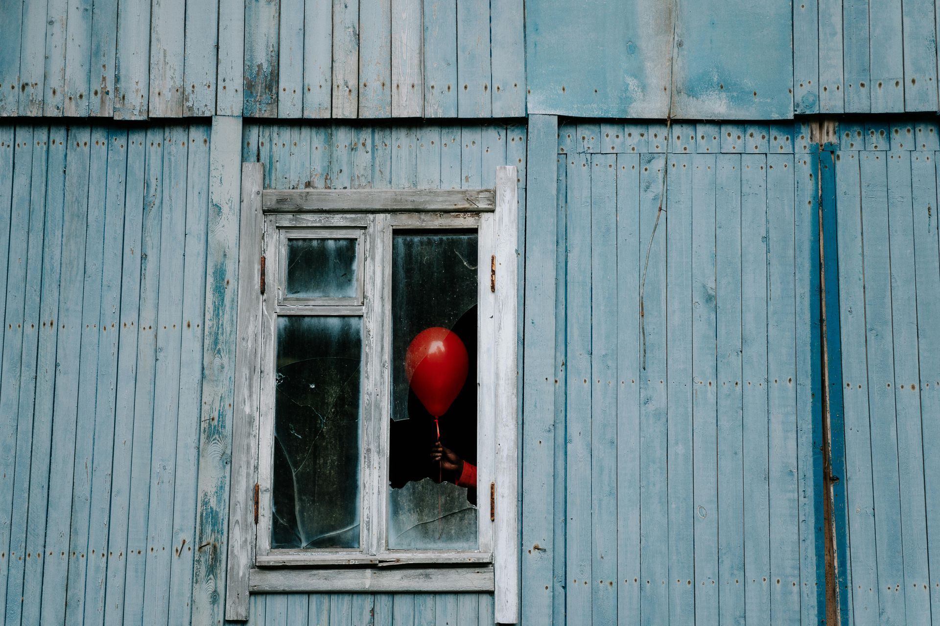 A red balloon is sticking out of a window of a blue wooden building.