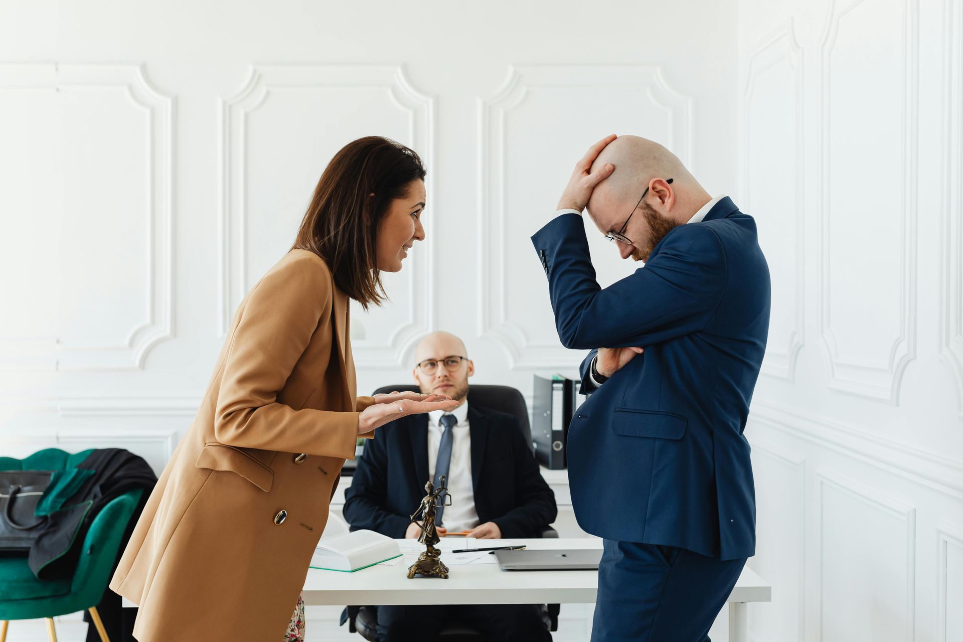 Woman in tan blazer argues with man in blue suit, lawyer in background.