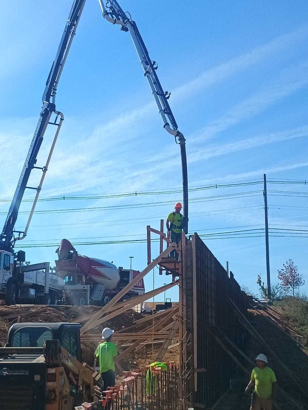 Construction workers pouring concrete into a tall wooden form using a pump truck under a blue sky