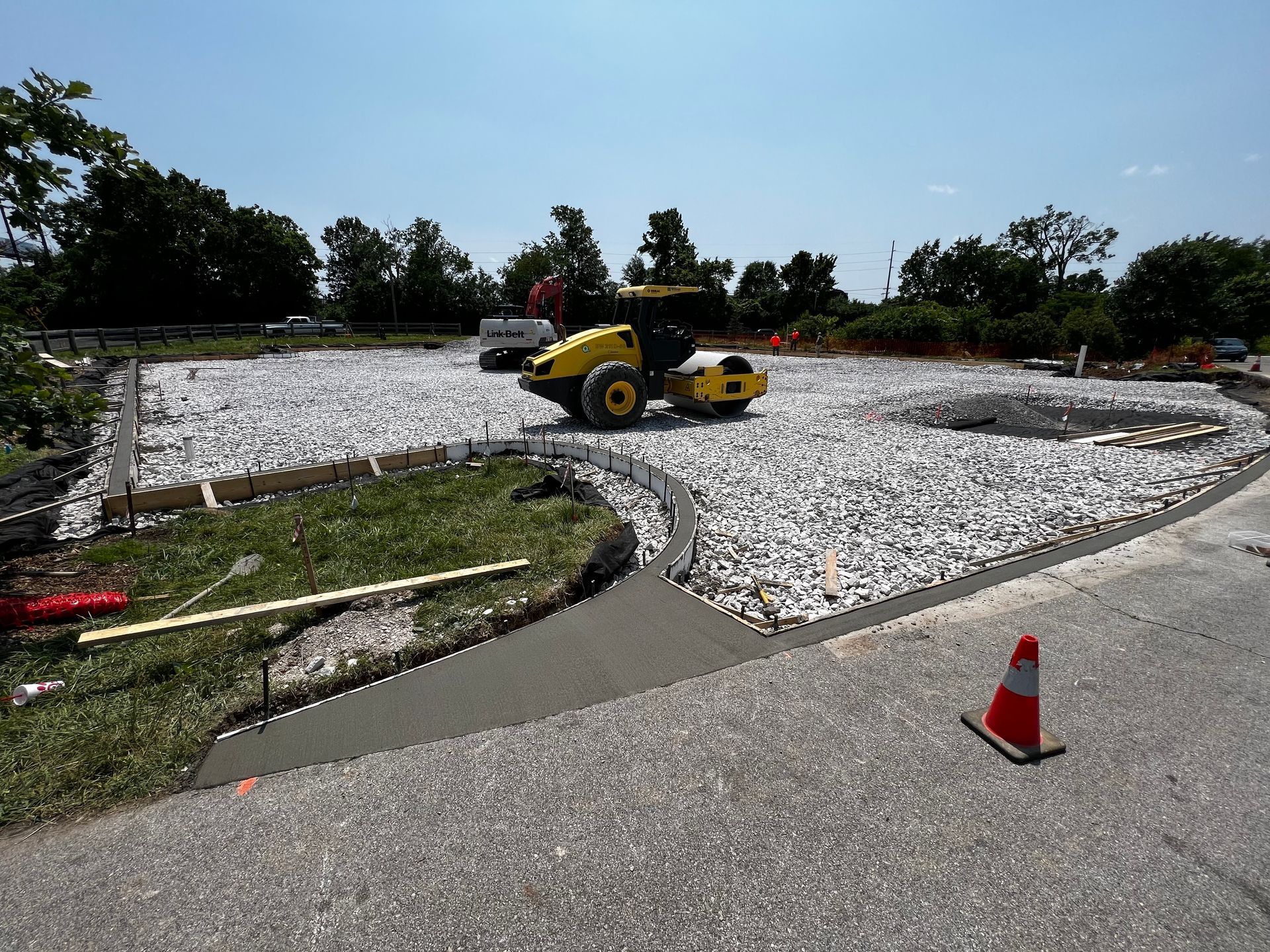 A construction worker in an orange vest and hat uses a vibrator tool to settle freshly poured concrete into metal rebar.