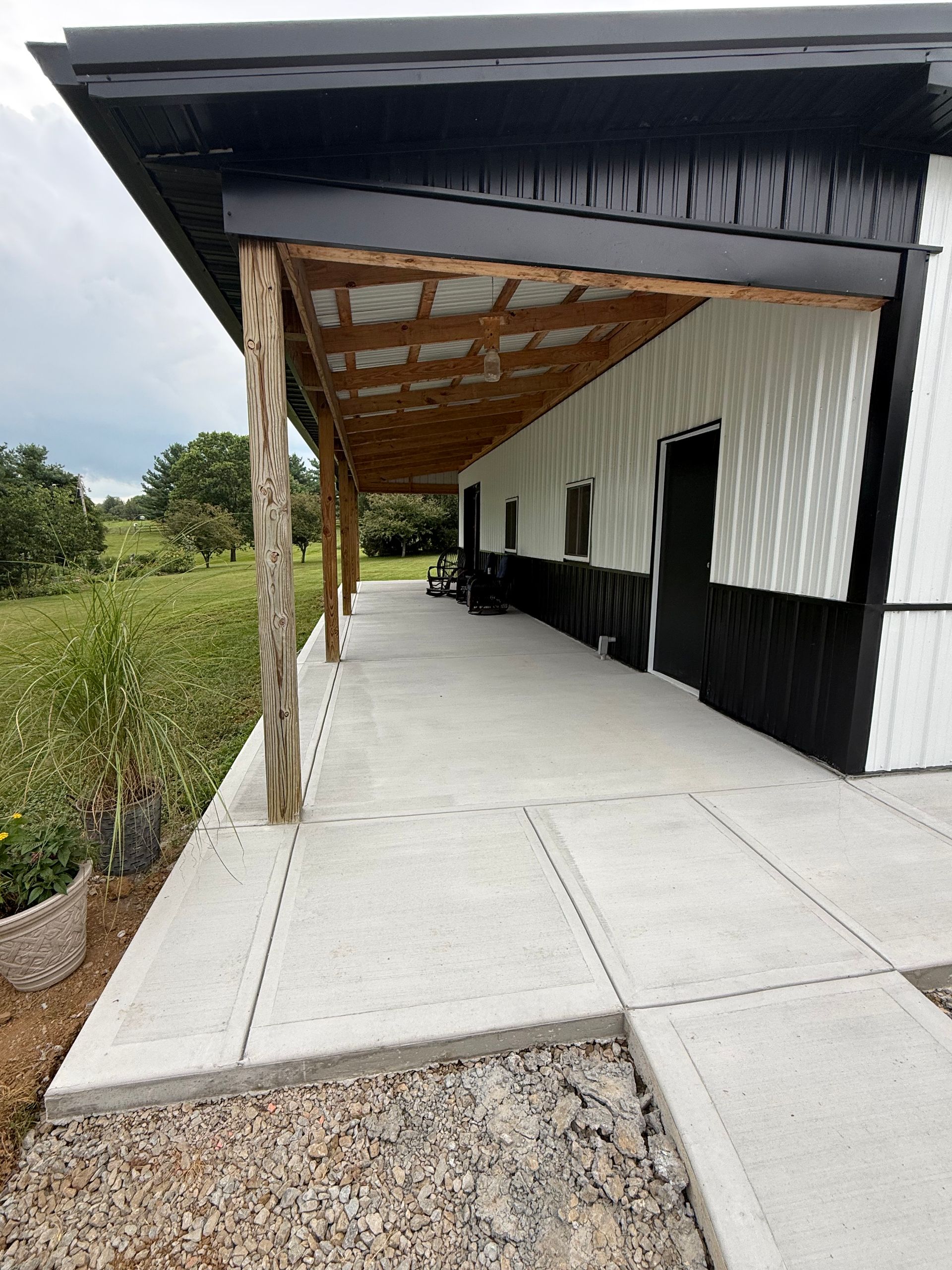 Covered concrete walkway beside a black-and-white building with open doors and a gravel path along the edge