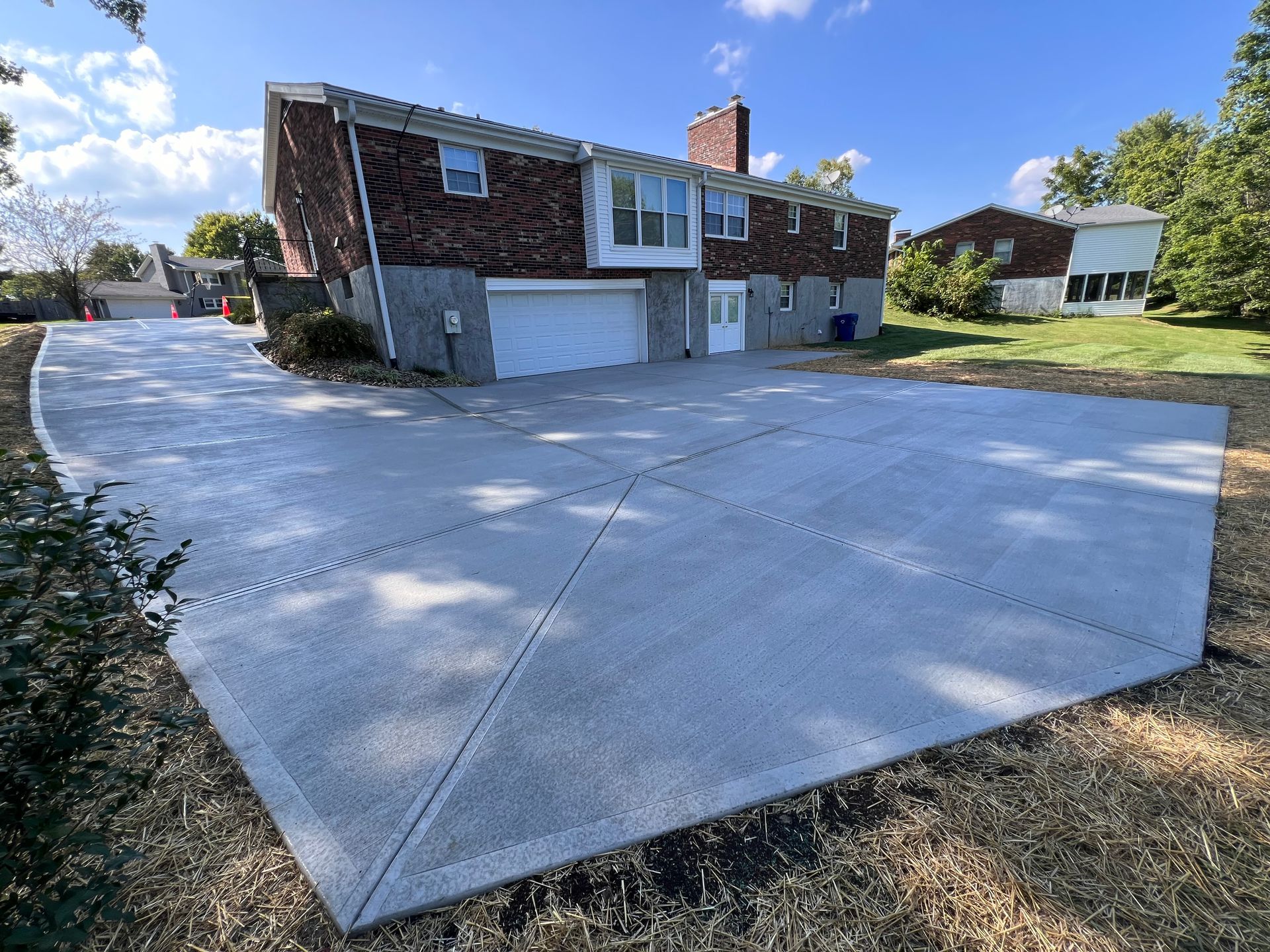 Suburban house with a large concrete driveway and attached garage under a blue sky