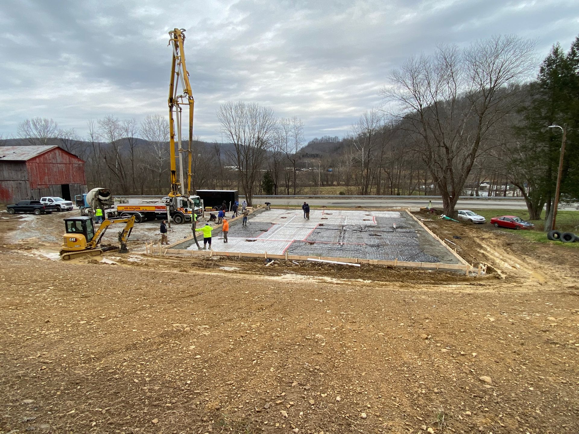 A worker in an orange vest uses a concrete vibrator to settle wet concrete poured onto a wire mesh grid.