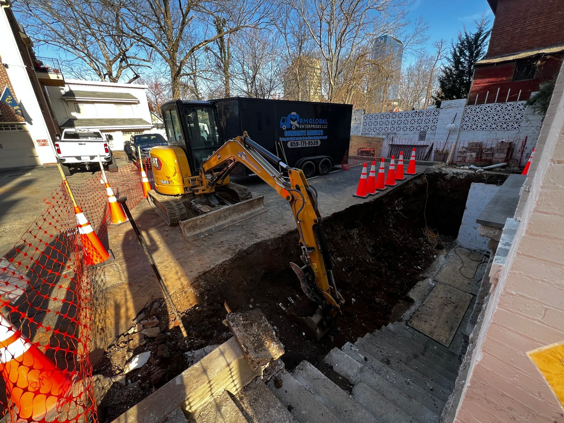 A person in orange gloves uses a long metal screed to level fresh concrete in a construction site setting.