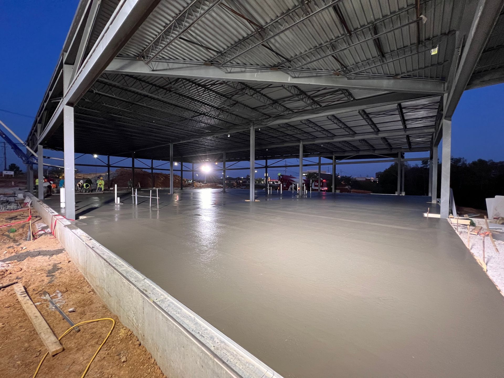 Flooded covered construction site with standing water under a large metal roof at dusk
