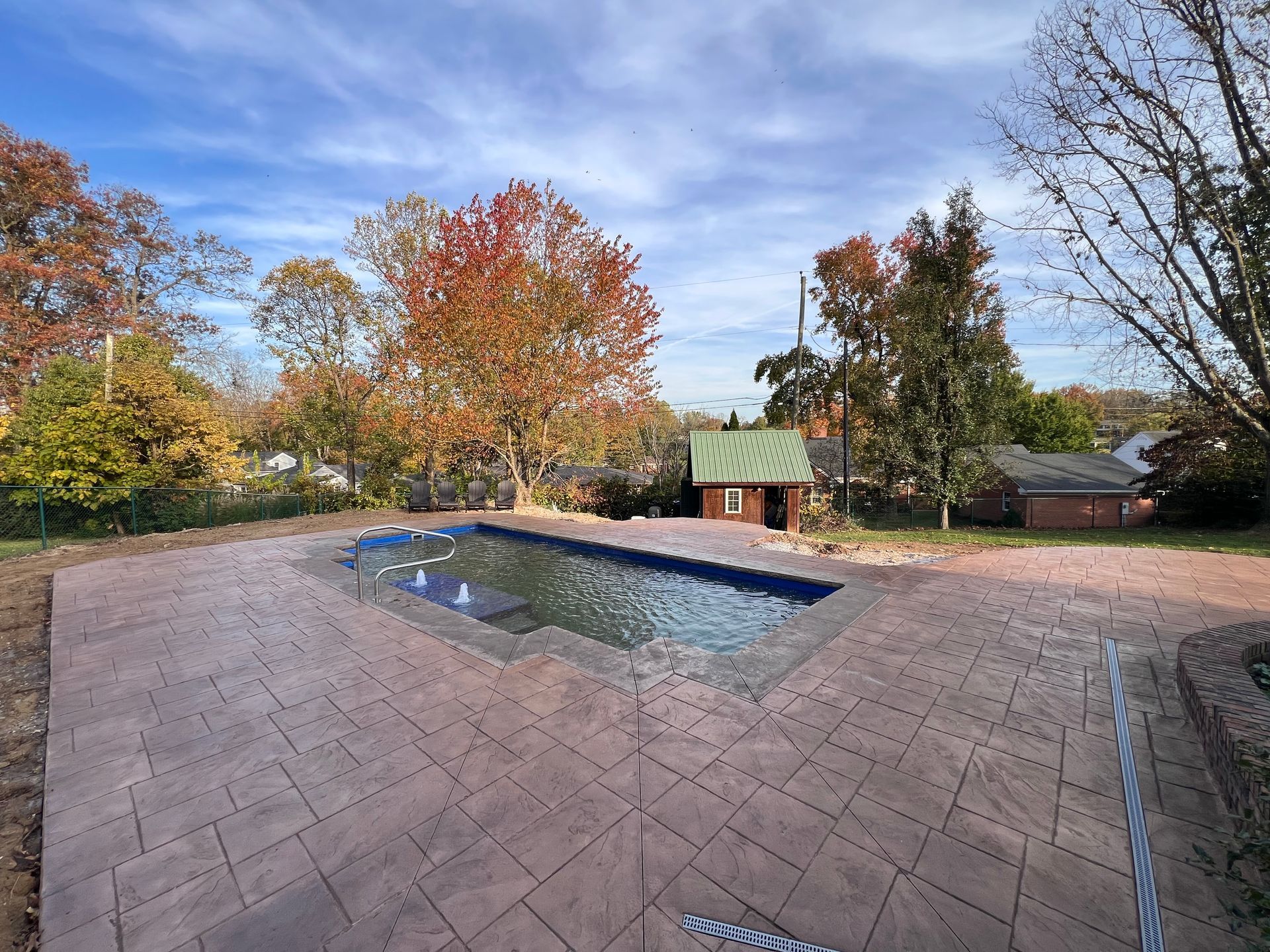 Backyard patio with a small covered pool or hot tub, surrounded by autumn trees and a stone deck.
