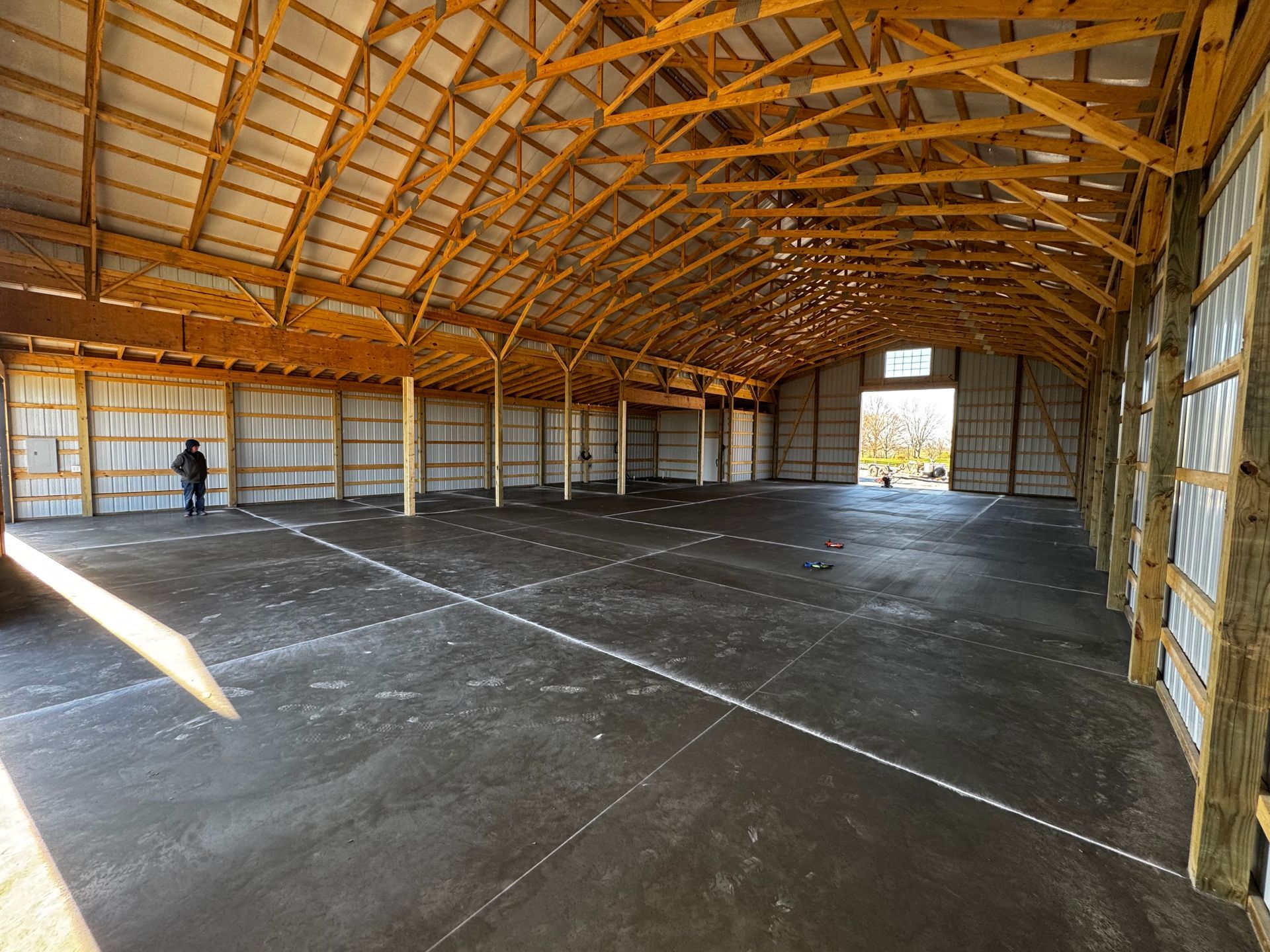 An unfinished, open-plan interior space with gray concrete walls, pillars, flooring, and large windows.