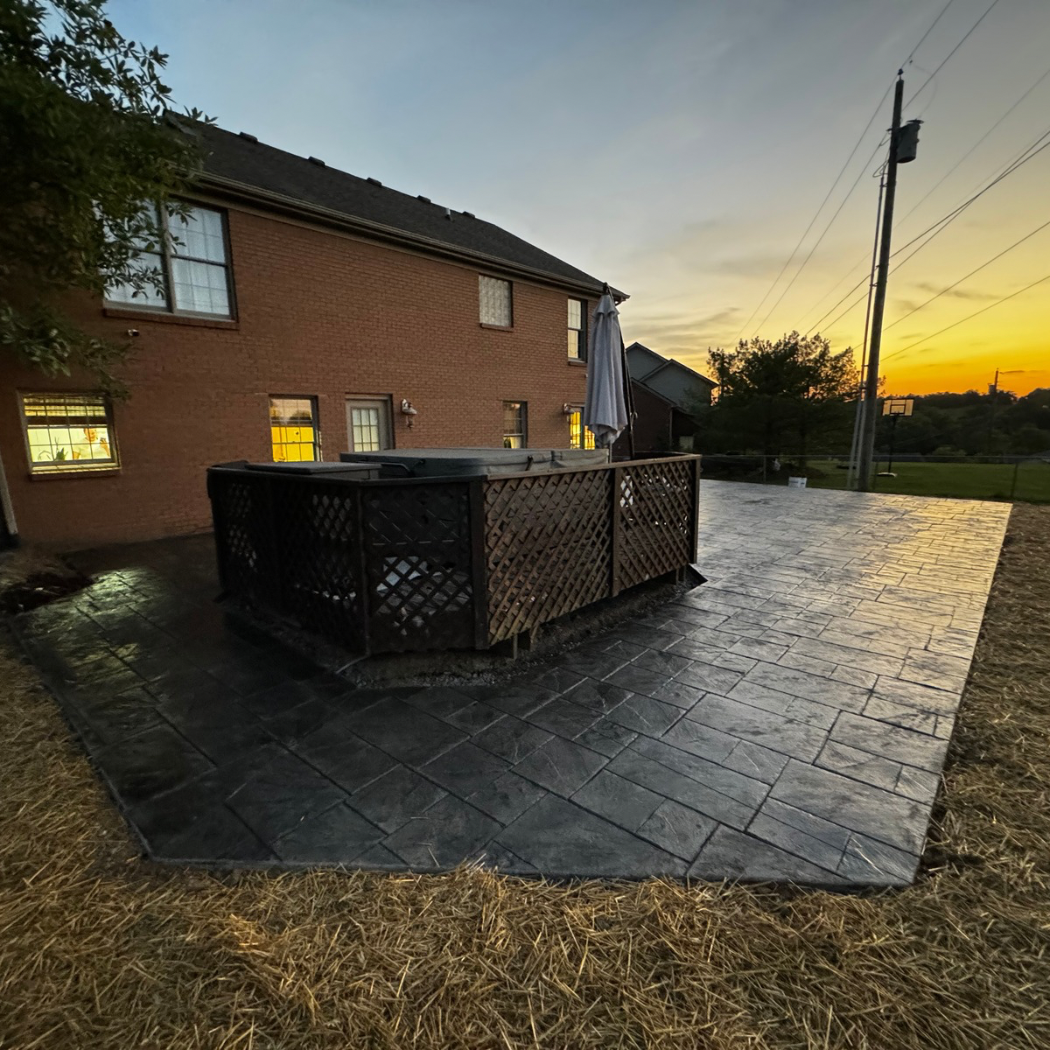 Brick house patio at dusk with wet black paving and a dark lattice enclosure in the center.