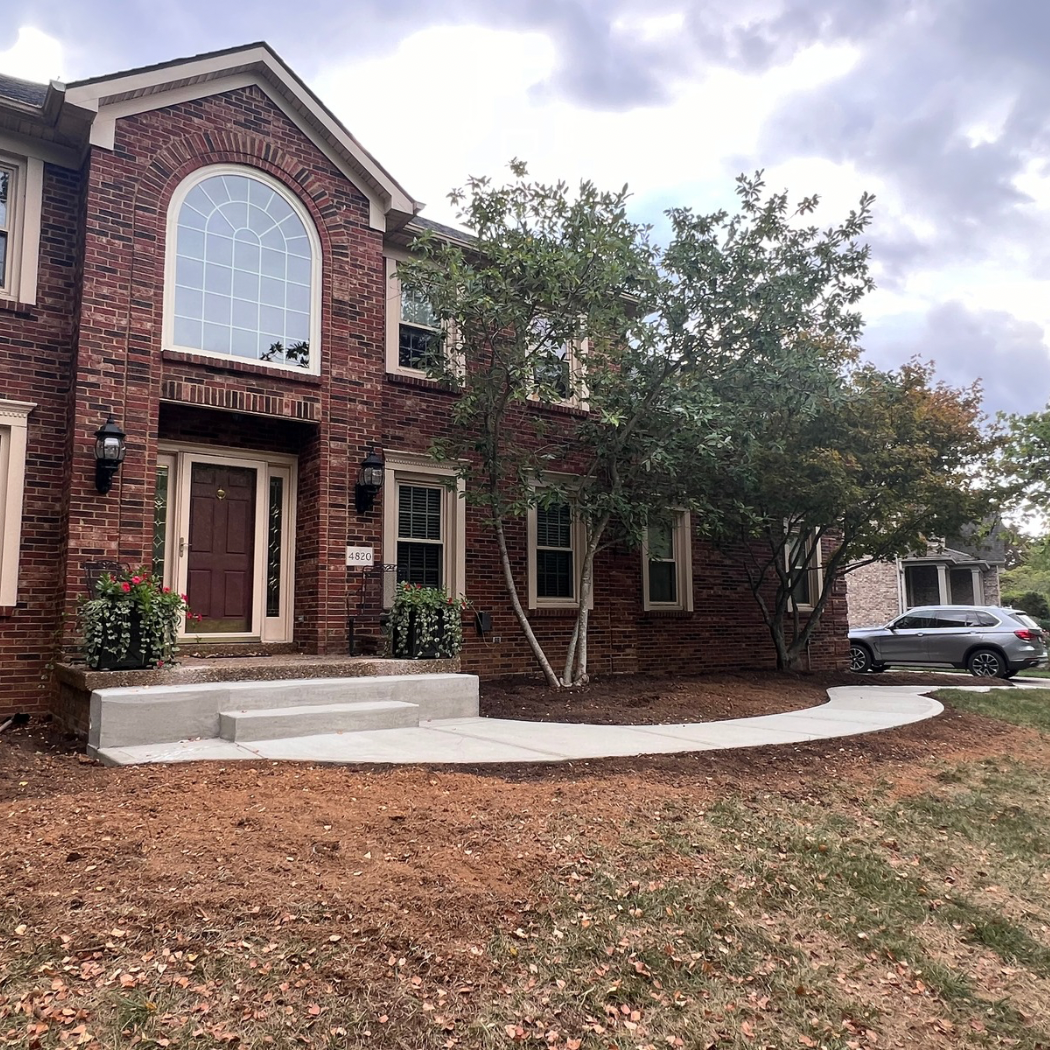 Brick two-story house with arched window, front steps, and a car parked in the driveway, surrounded by fallen leaves