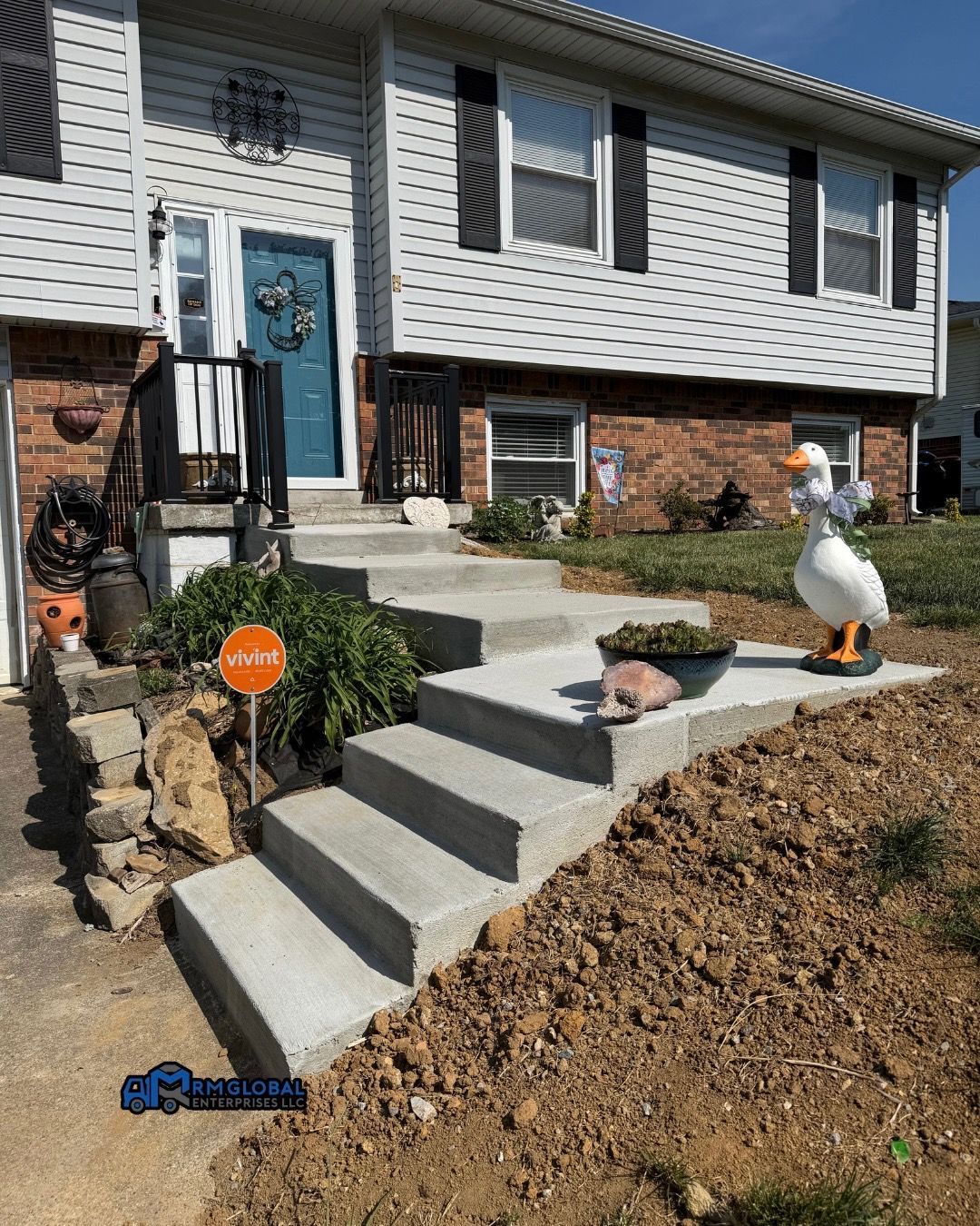 Front yard with concrete steps, brick house, blue door, and a white goose lawn ornament.