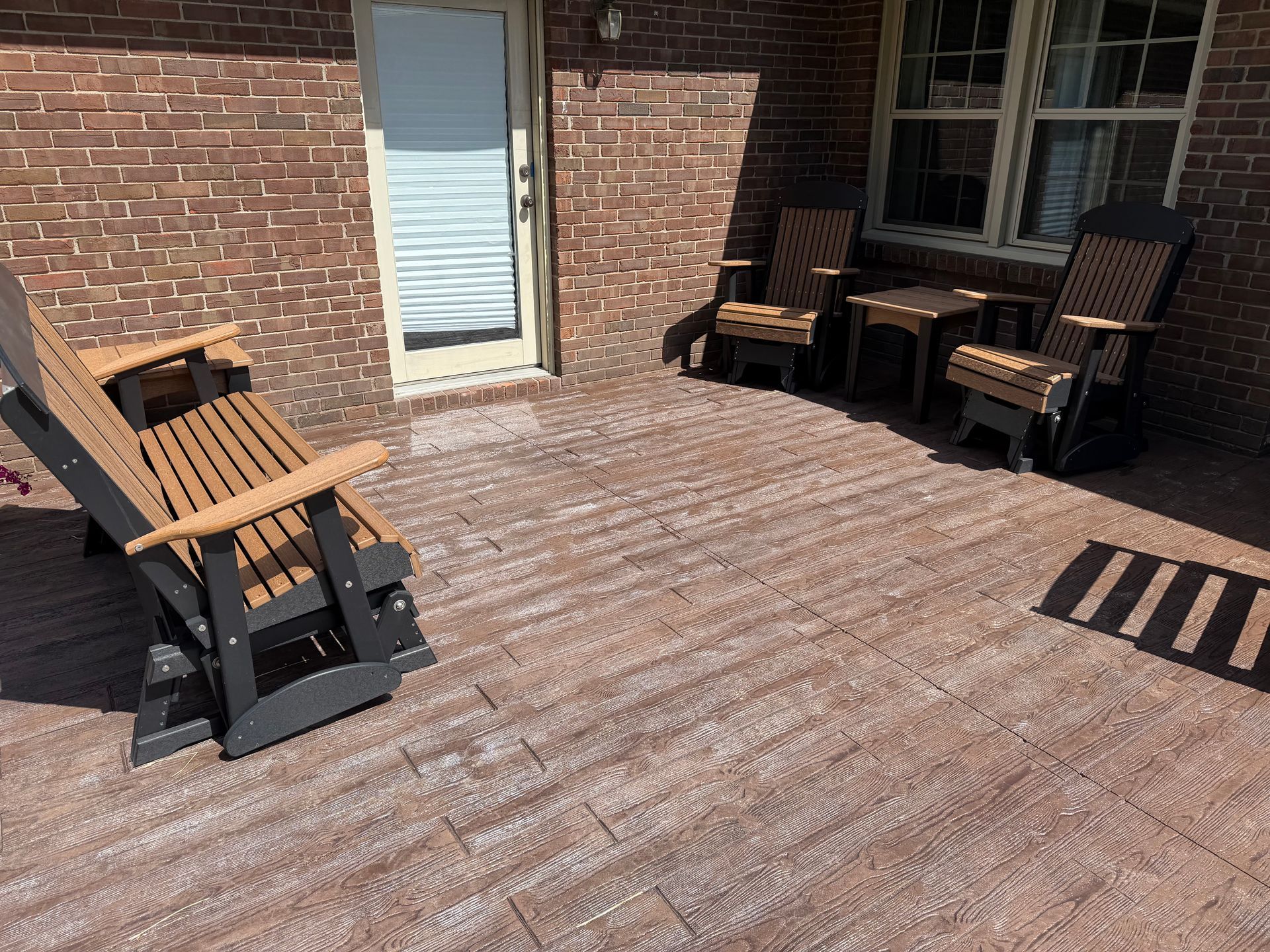 Brick patio with wooden Adirondack chairs and a glass door against a brick house.