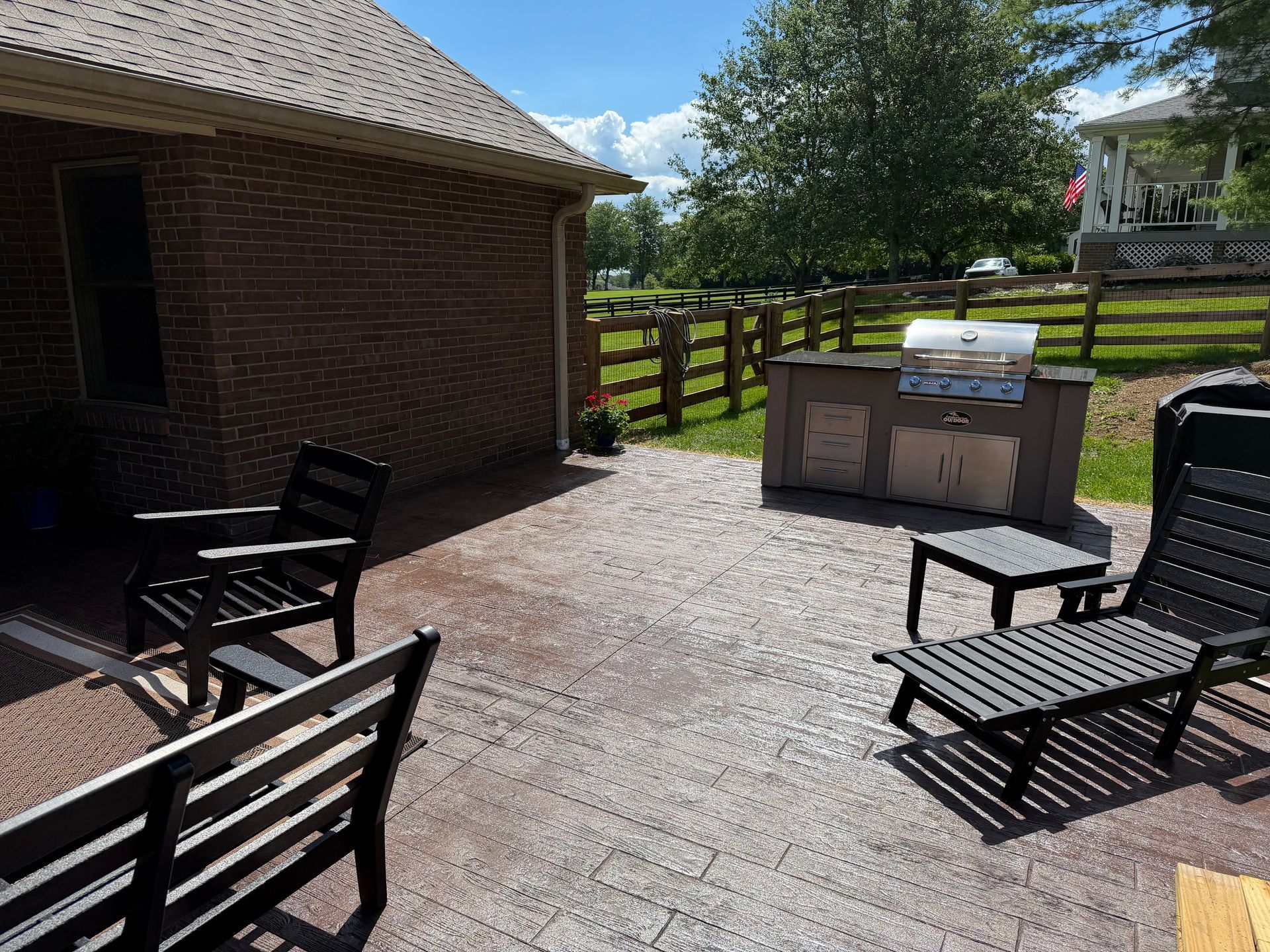 Brick patio with black chairs and a grill beside a brick house and fenced yard