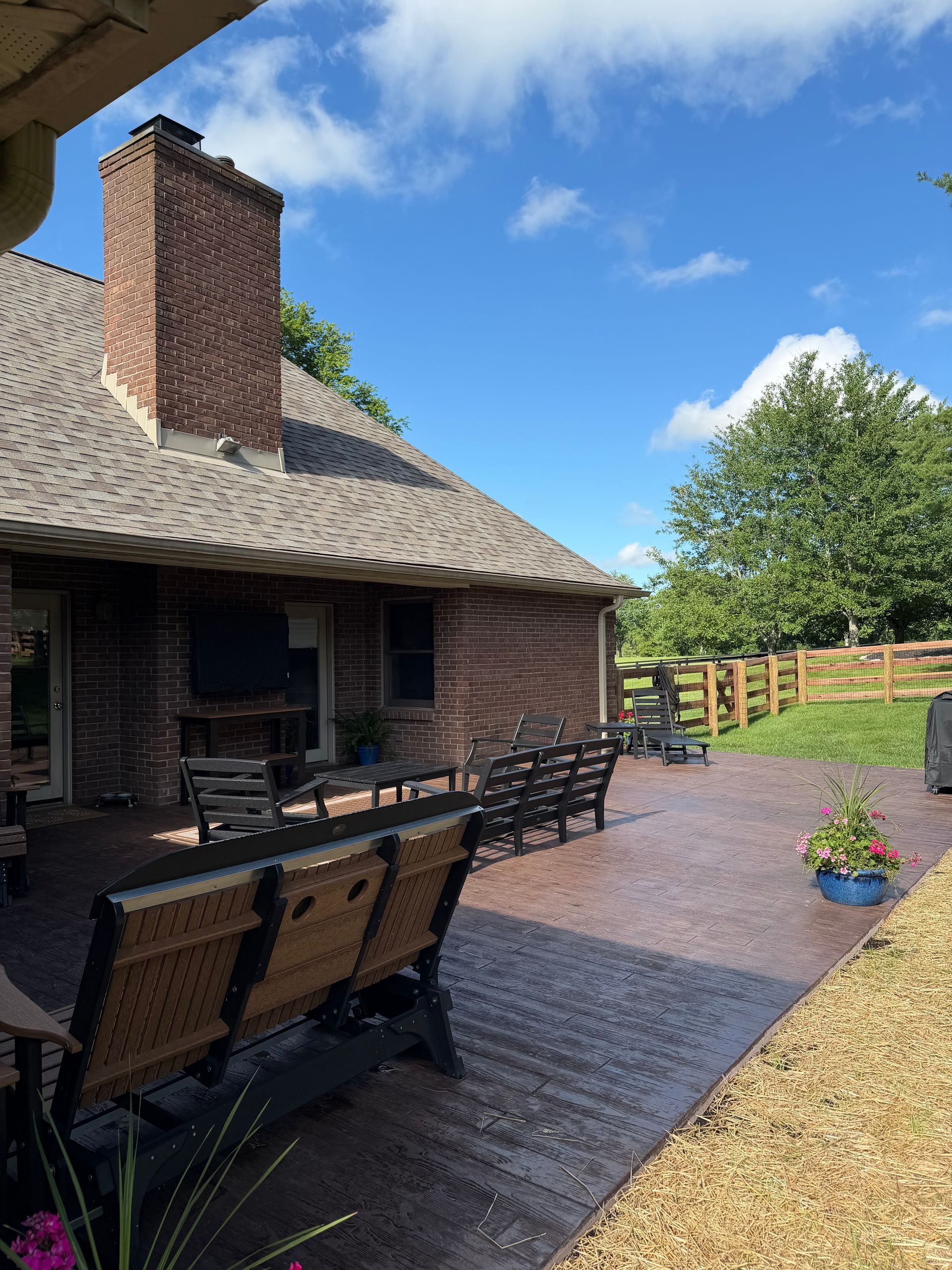 Brick house patio with outdoor dining table, brick path, potted flowers, and a green lawn under a blue sky