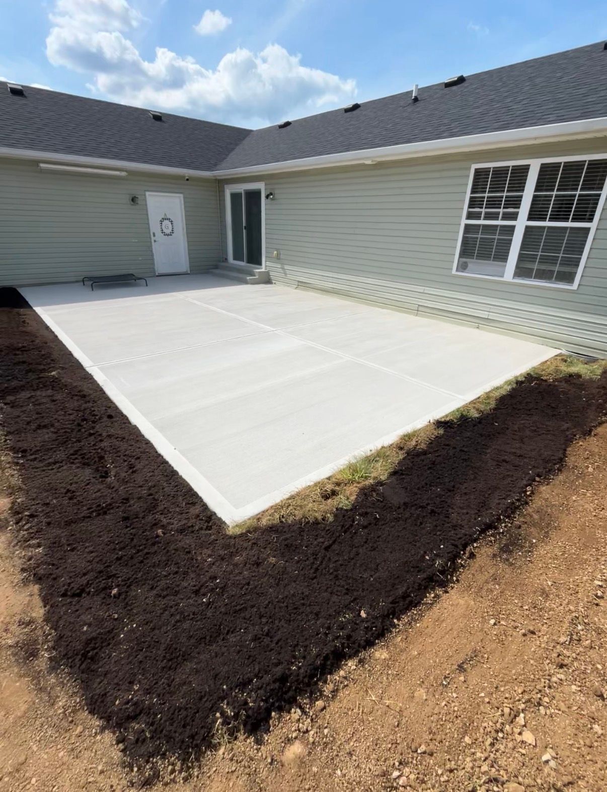 Freshly poured concrete patio beside a house with dark mulch edging and beige siding