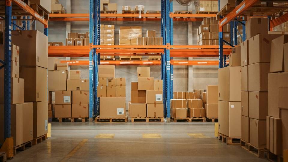 Warehouse aisle with stacked cardboard boxes on pallets and orange-blue shelving units