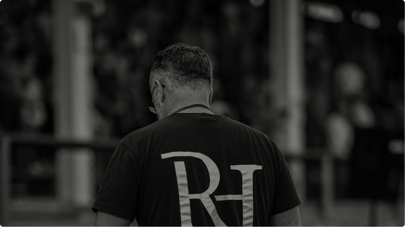 Man in black shirt with large “RH” logo, seen from behind in a blurred indoor setting