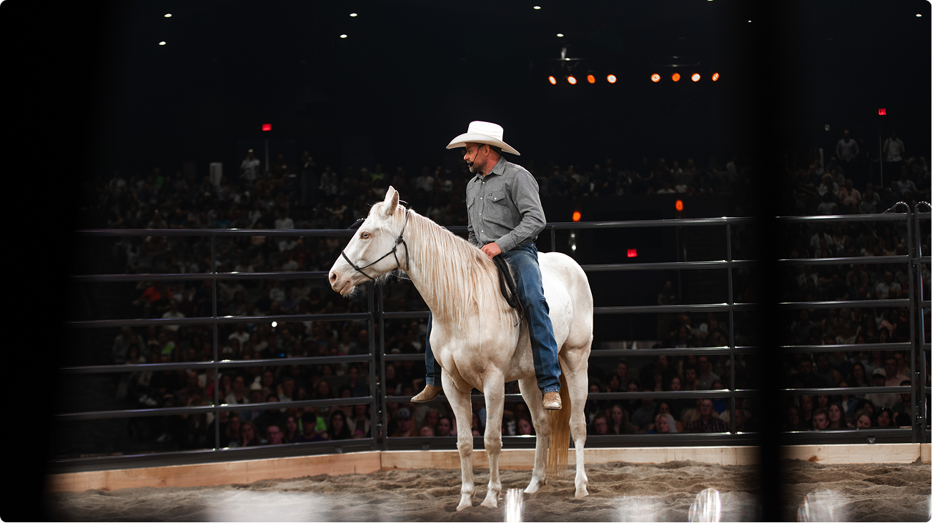 Cowboy in a white hat riding a white horse in a dimly lit rodeo arena