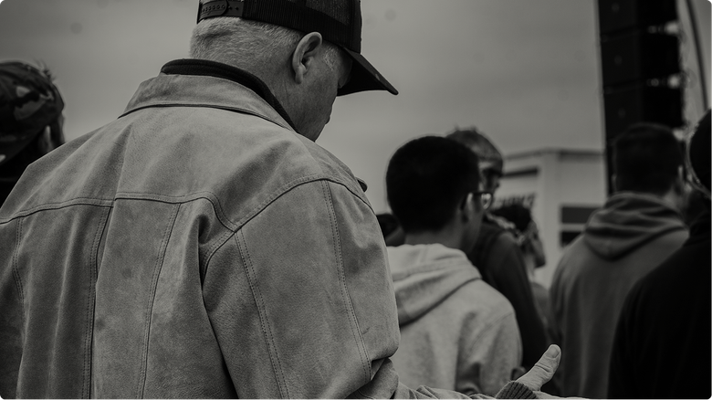 People standing in line indoors, seen from behind, one person in a cap and denim jacket in the foreground