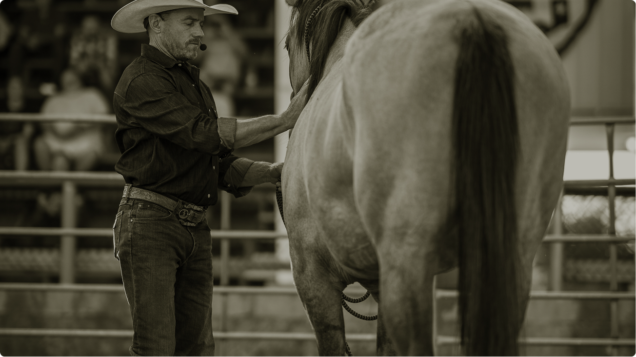 Cowboy in a hat standing beside a horse in an indoor arena
