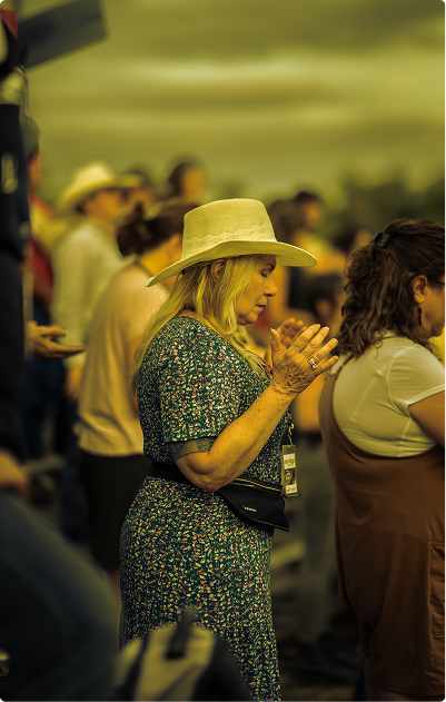 Crowd at an outdoor event; a woman in a hat claps while others stand nearby