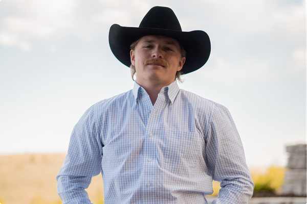 Person in a black cowboy hat and light blue shirt standing outdoors against a bright sky.