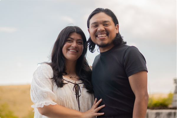 Two people smiling and embracing outdoors in a grassy field at sunset
