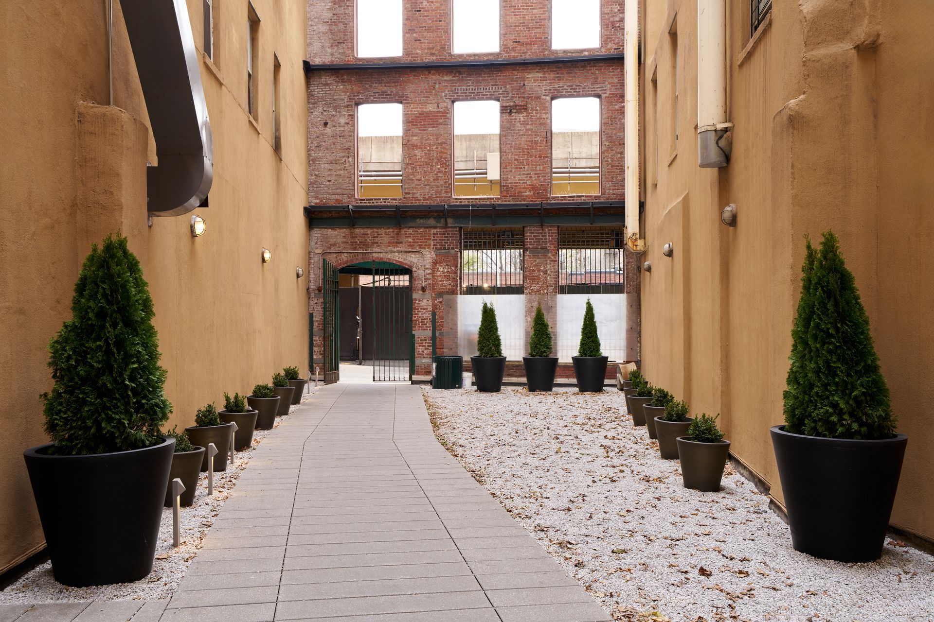 Narrow alleyway with paved path, brick facade, and potted trees.