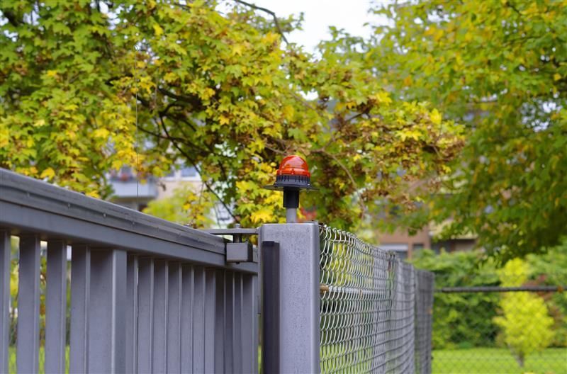 Security gate with red warning beacon on metal fence providing enhanced outdoor property protection.