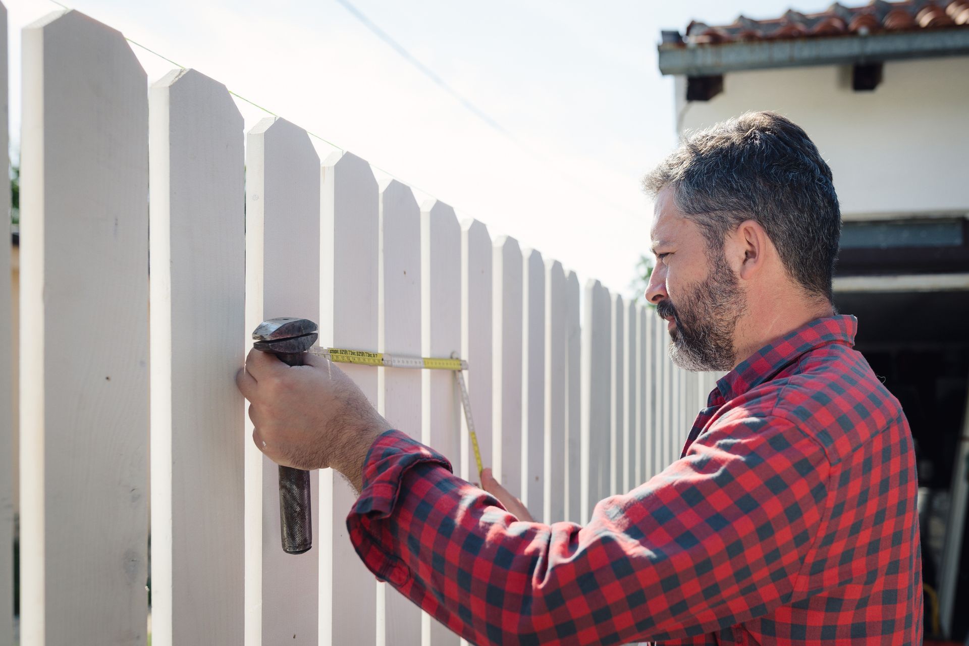 A man measuring a white fence with a tape measure, representing a professional fencing company. A man measuring a white fence with a tape measure, representing a professional fencing company.