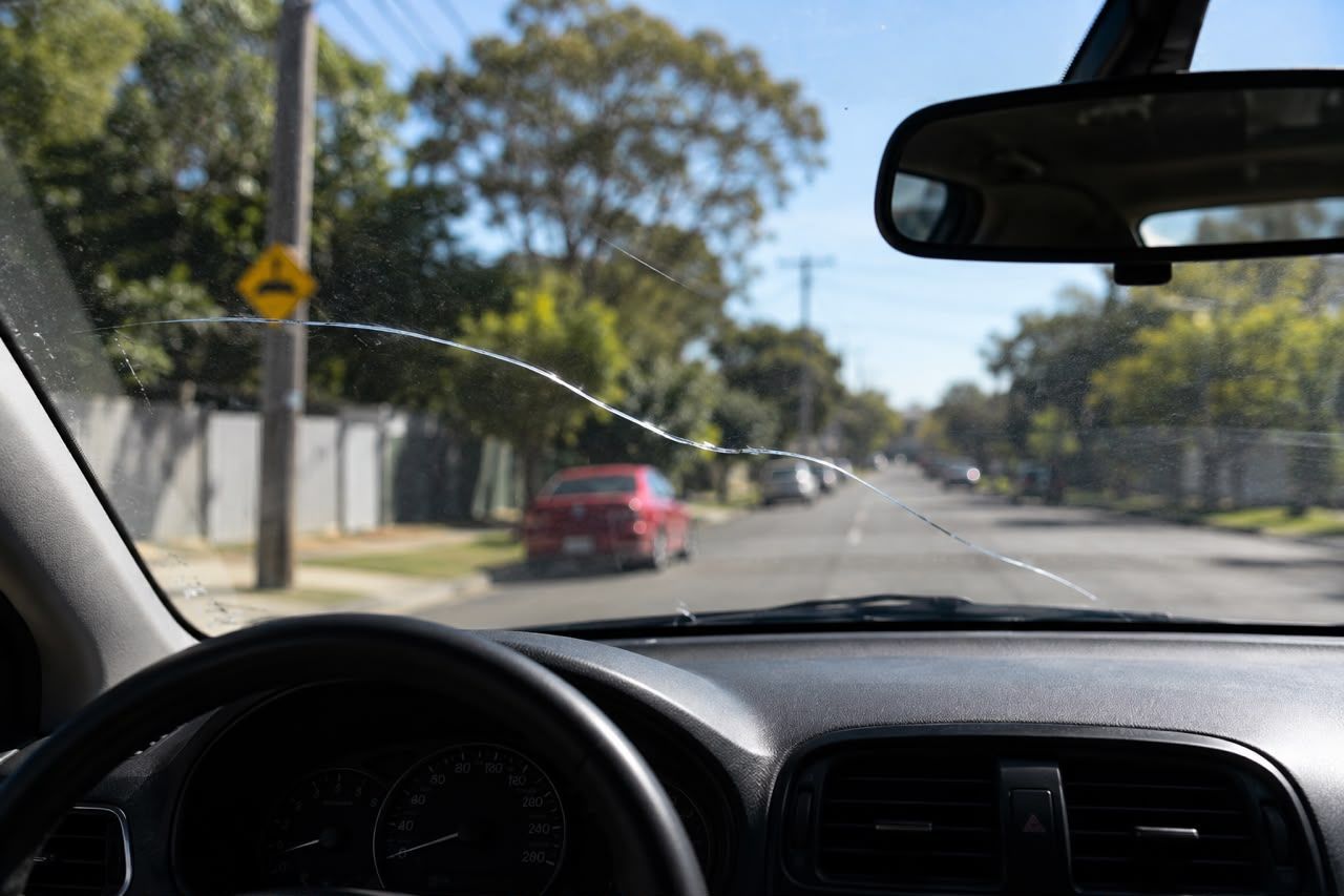 View from a car windshield with a cracked glass, driving down a sunny residential street