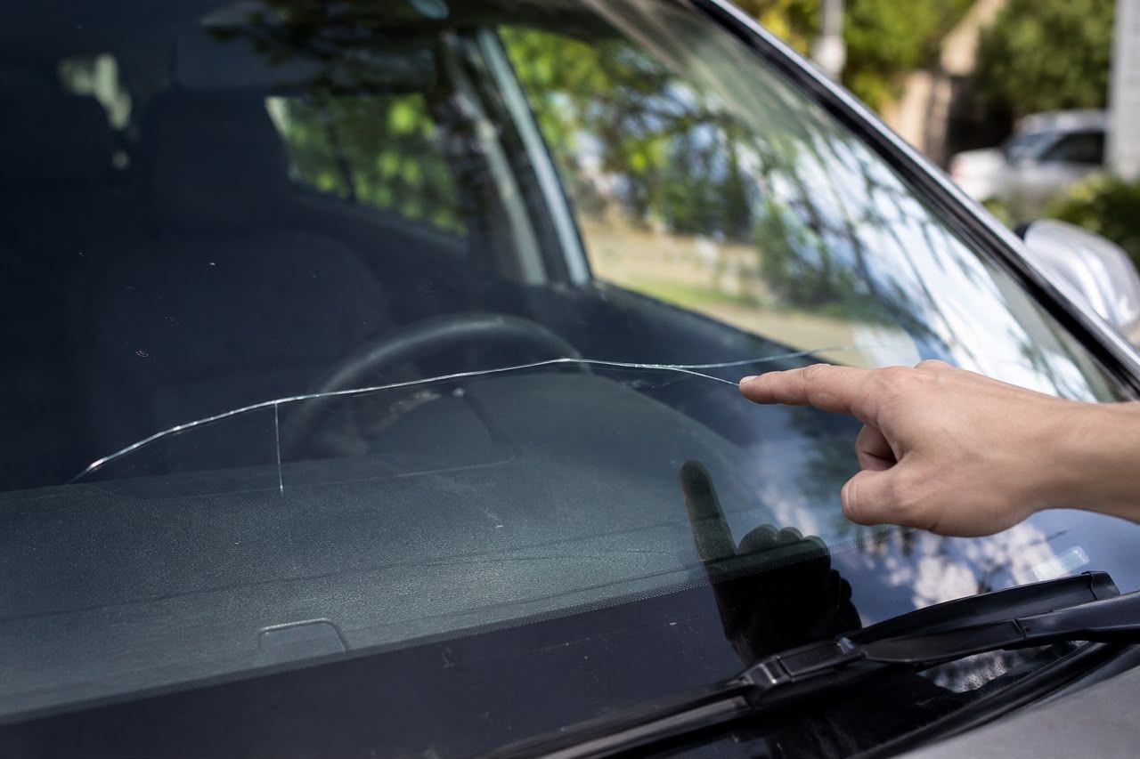 Hand pointing at a cracked car windshield